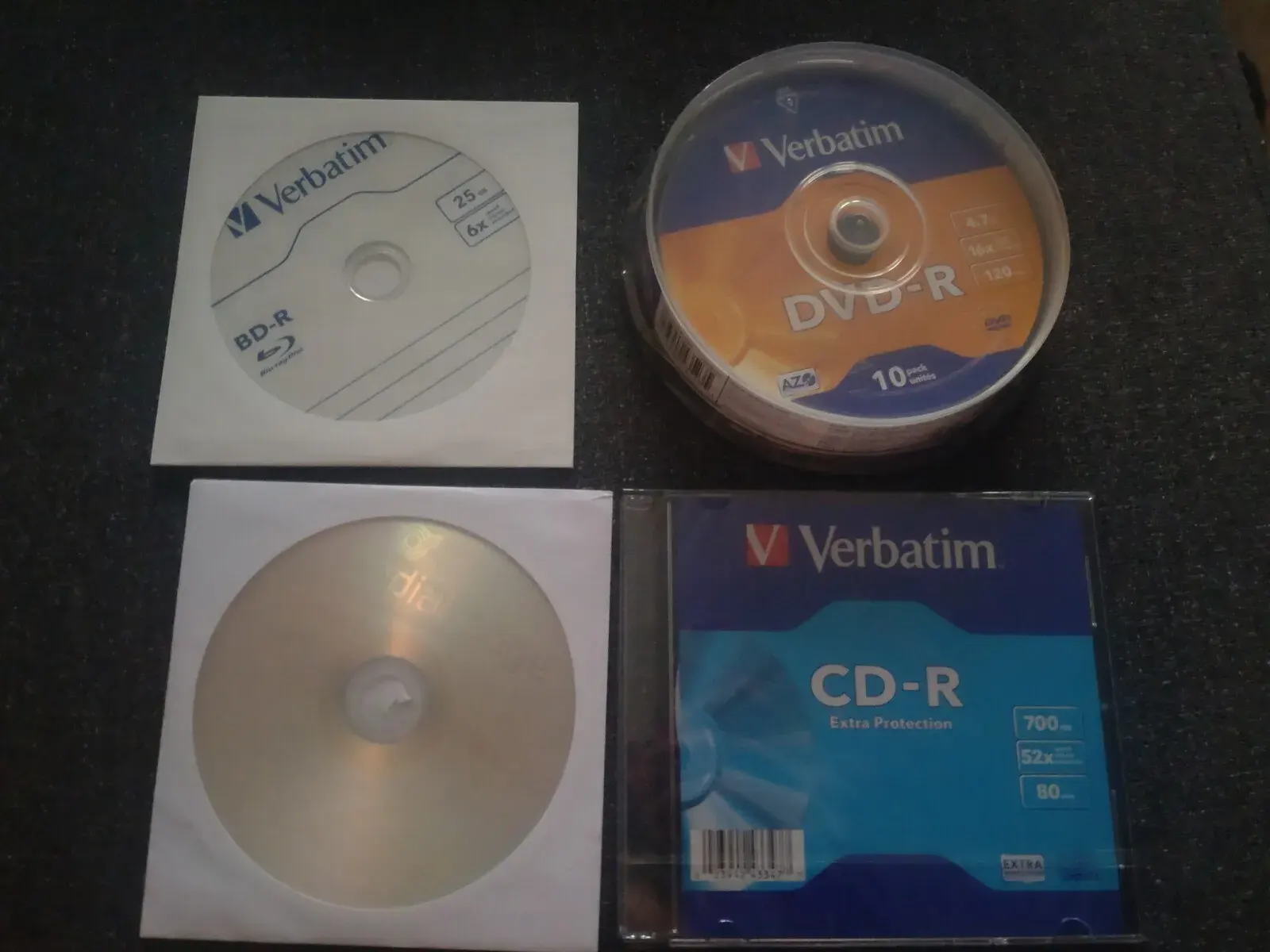 A bunch of optical discs: top-left: BD-R with 25GB and 6x reading speed in a paper sleeve top-right: a "cake box" of 10 DVD-Rs with 4.7GB bottom-left: a DVD-R with 4.7GB in a paper sleeve bottom-right: a CD-R with 700MB in a plastic packaging